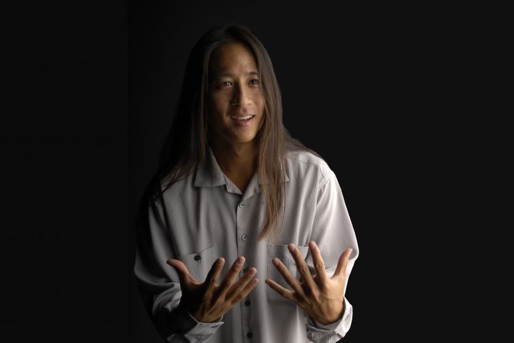 Kealoha Wong in front of a black backdrop with his hands out in front of him 
