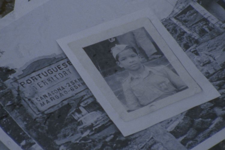 Black and white images appear on top of one another. The smaller one on top features a young boy in a uniform. Beneath that is a larger one of a sign that says "Portuguese Territory" and an old car. The photo appears damaged.