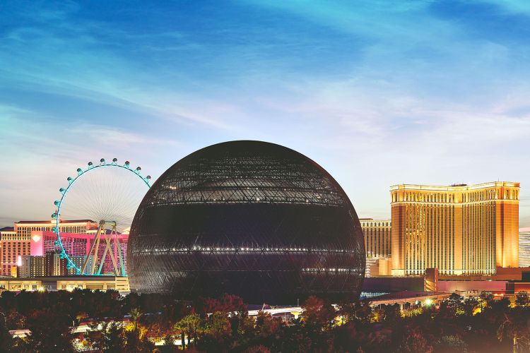 A large black sphere dominates the Las Vegas skyline. A Ferris wheel is on the left in the background, and other buildings can be seen as well. The sky is blue, but the foreground is dark.