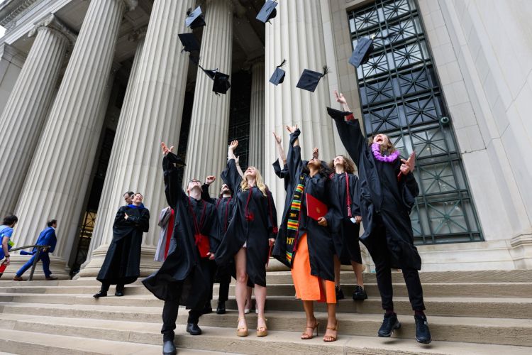 A group of graduates toss their caps into the air on the steps of Killian court