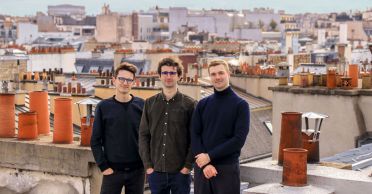 Raber, Levi, and Cousin stand together on a roof. In the background are the roofs of Paris, with many orange chimneys.