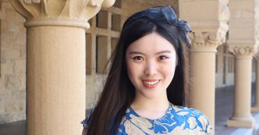 Portrait of Carina Hong with ribbon in her hair and columns in the background. 