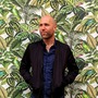 Portrait: Matt Stempeck in front of a mural of green leaves and plants