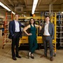 Three people in business attire posing in a warehouse 