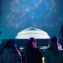 Four people with their backs facing the camera looking at the MIT dome on Killian Court at night with lights in the sky 