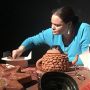 Erin Genia is shown from chest up leaning over an array of clay artwork, including a teapot and a large star.