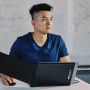 Jack Yao is shown at a table with a small computer screen in front of him. It has an extended display. A whiteboard is behind him.