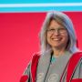 MIT President Sally Kornbluth smiling, in MIT robes, from chest up with red and blue background.