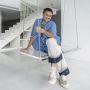 Parmesh Shahani sits on a swing in a spare white room with white steps in the background. He wears a blue shirt and white pants.