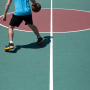 A basketball player is shown from the midriff down on a green court with a red circle.