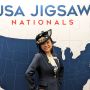 A photo of Tammy McLeod standing in front of a backdrop that says USA Jigsaw Nationals with a map of the US under the words