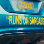 A photo of a blue car's bumper with the words "runs on sargassum" on it 