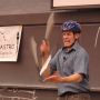 A photo of David Rush in a classroom with a blackboard behind him wearing a helmet and juggling knives