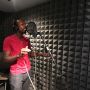 Kelvin Frazier is shown in a recording booth singing into a microphone. The wall shows soundproofing.