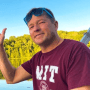 Headshot of Andy Obst ’90 waving while on a boat, sunglasses perched on his head. He's wearing an MIT t-shirt