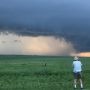A landscape with a twister in the distance and a man taking a photo