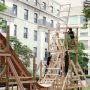 A photo of a wooden roller coaster structure outside in a courtyard with building surrounding it