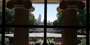 Pillars of Killian court frame a view of the commencement ceremony with the Boston skyline in the background