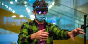 Man in a green plaid shirt wearing VR goggles and a mask 