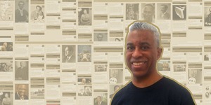 Ken Granderson stands in front of a collage of Black History facts from his website