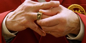 A man in a red suit jacket putting his brass rat MIT alumni ring on his finger