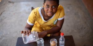 A young child leaning on a table pouring liquid from one container to another