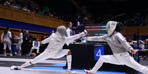 A photo of MIT alum Kristen Palmer at an indoor fencing competition in a fencing suit facing an opponent
