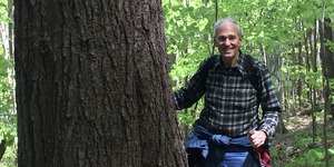In hiking clothes, Bill Moomaw stands beside a tree trunk in the forest