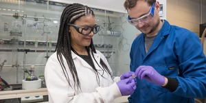 Woman in lab with gloves and lab coat holding object with man in lab 