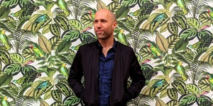 Portrait: Matt Stempeck in front of a mural of green leaves and plants