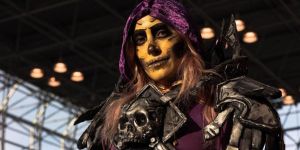 Emma Kay in costume, from chest up. She wears a purple hood, yellowish makeup, and a skull breastplate.