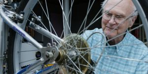 Neal Carlson is shown through the spokes of a bicycle. He is looking at the gears.
