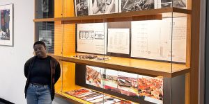 Deborah Tsogbe stands to the left of a large display case in the MIT Rotch Library