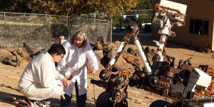 MIT alum Louise Jandura in an all white suit talking to a colleague on a rocky service with a rover/machine