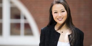 A photo of Sophie Bai standing outside with a brick wall behind her with a large cutout semi-circular window