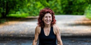 A photo of MIT alum Lillian Cuthbert in a crosslegged pose elevating her legs above pavement with trees behind her