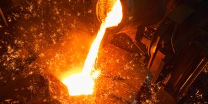 White-hot steel is shown being poured from a pipe into a receptacle. Sparks fly.