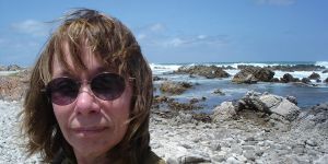 Darleen Ketten is shown in closeup, wearing sunglasses. A beach scene is behind her.