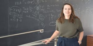 Alex Reiss-Sorokin stands in front of a blackboard full of equations.