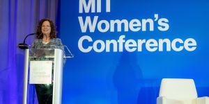 Photo of MITAA President Natalie Lorenz-Anderson standing at a podium during the MIT Women's Conference with the blue branding in the background