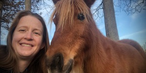 Sarah Low selfie with a reddish brown horse against a background of trees and blue sky