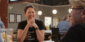 Jennifer Yang stands in her craft distillery's tasting room in Westminster, Maryland. She smiles with her elbows on the bar and her hands clasped. Behind Yang, you can see more of the restored historic venue. You can glimpse part of the company t-shirt Yang is pictured wearing. Vertically it reads, "Westminster." Horizontally it reads, "Moved for love, stayed for whiskey." 