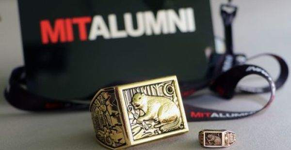 Pictured Large rendering of a Brass Rat next to a small brass rat, with the MIT Alumni Logo in the background.