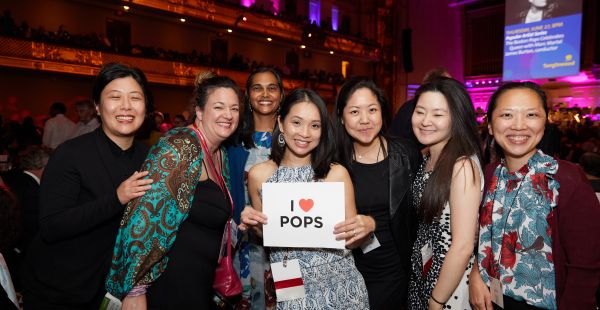 Image: Group of seven alumni posing in Symphony Hall holding a sign that reads I Heart Pops