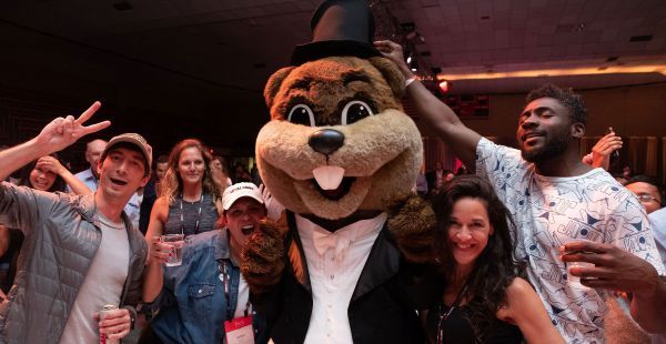 Image: group of four alumni posing with Tim the Beaver mascot who is dressed in a tuxedo