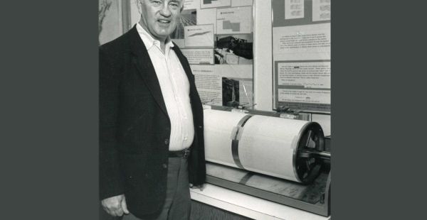 A black and white photo of alum Lynn Sykes standing next to a spherical piece of equiptment.