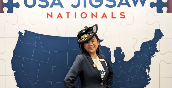 Tammy McLeod '99 standing in front of a wall designed to look like a puzzle of the map of the united states reading USA Jigsaw Nationals