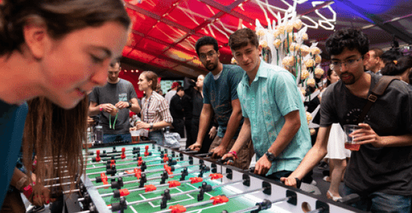 Group of alumni playing foosball inside a large multi-colored event tent.