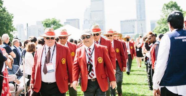 Image: MIT 50th reunion attendees in red jackets walking into Commencement with the Boston skyline behind them.