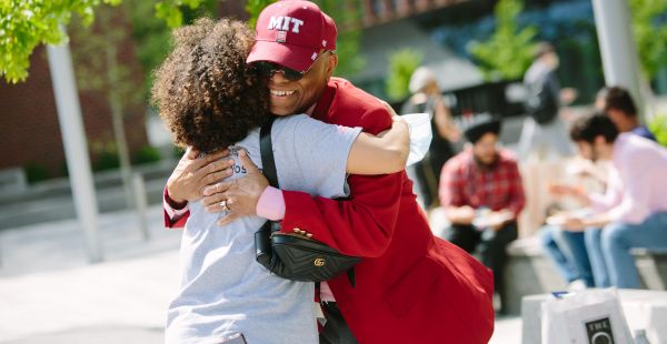 Two alumni, one in a red jacket, hugging